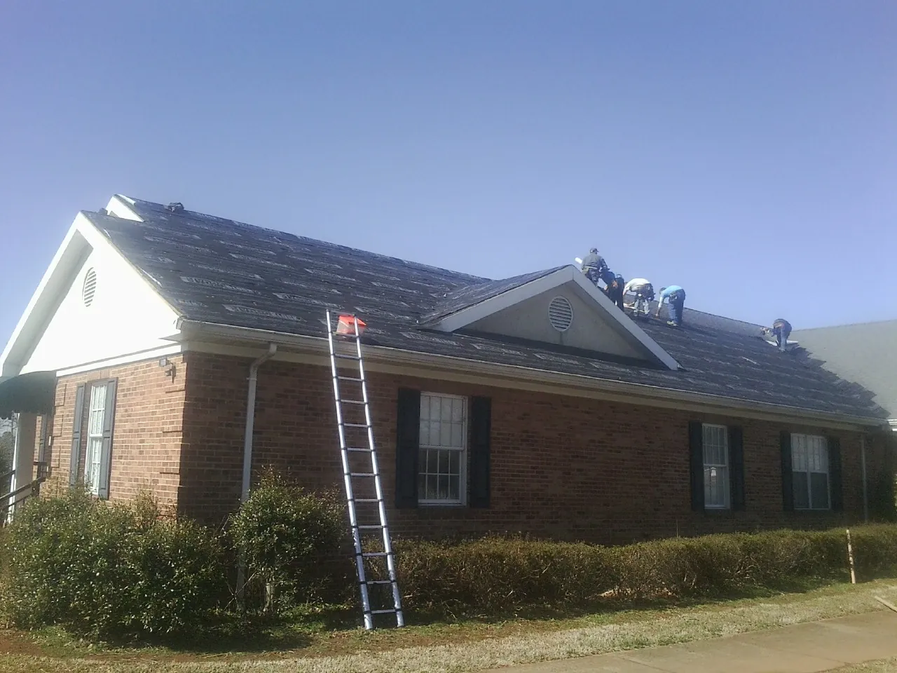 Crew tearing shingles off a brick ranch roof with a ladder set — Emergency Roof Repair work by our crew in Pegram