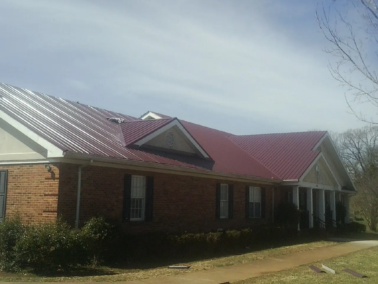 Red metal roof with gabled entries on a long brick building, from a Hail Damage Roof Repair job in Pegram