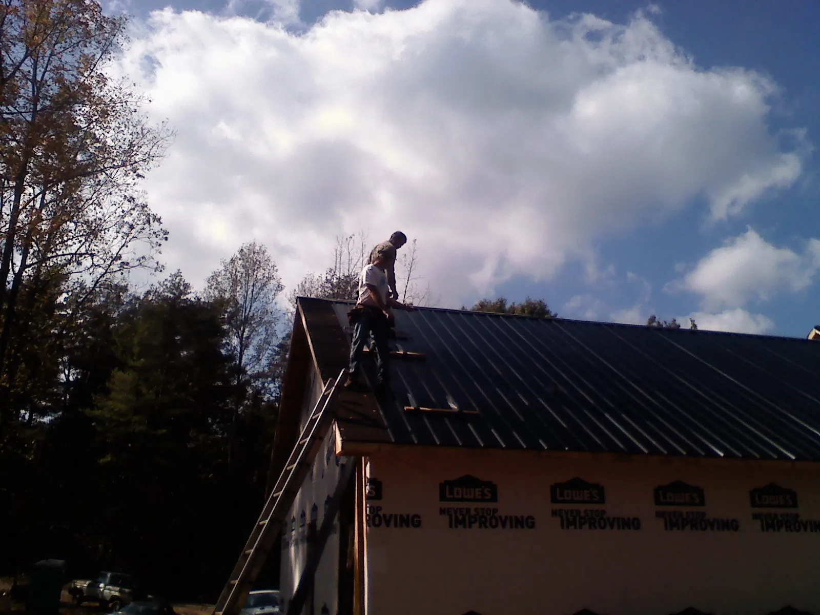 Roofer fastening dark metal panels high against a cloudy sky, from a Roof Inspection job in Pegram