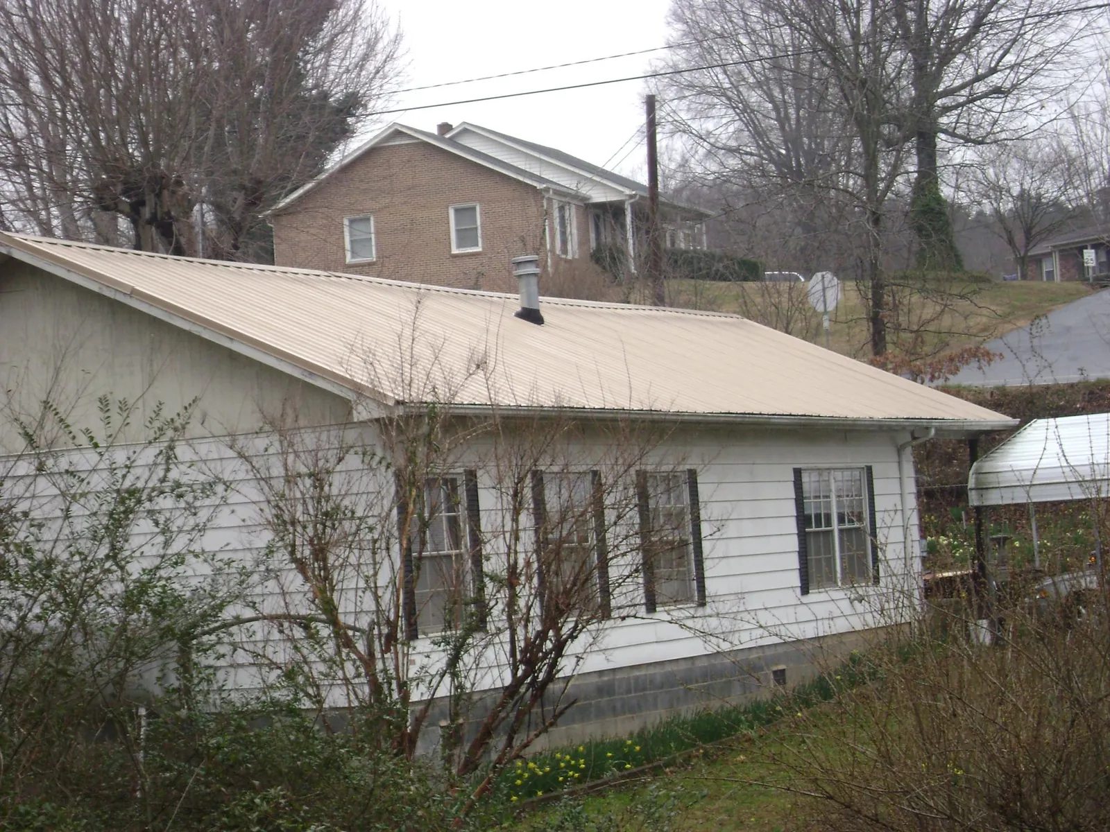 Tan metal roof on a white sided house set into a hillside — Commercial Roofing by Roofing Brothers in Pegram